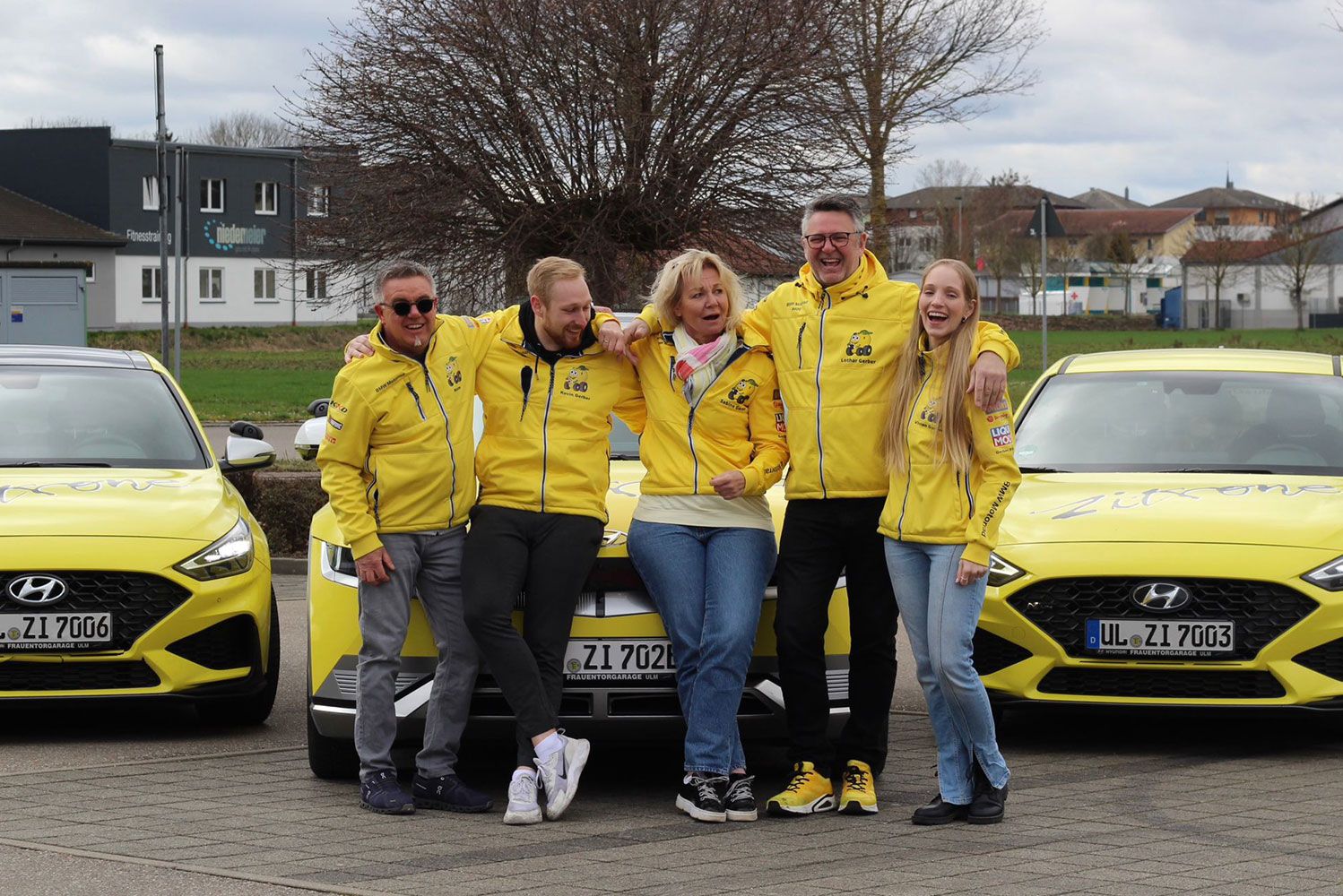 Fahrschulteam steht gemeinsam vor einem Fahrschulauto